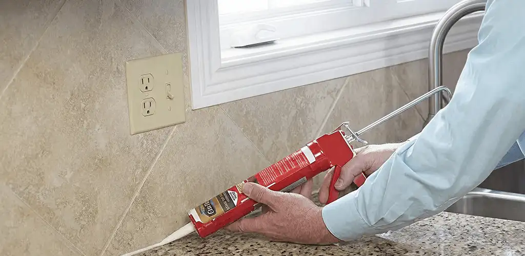 Handyman applying caulk along a kitchen backsplash and countertop seam in Lakewood, CO