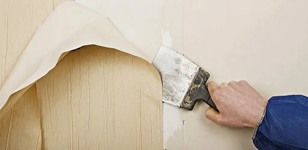 Handyman removing wallpaper with a scraper for wall preparation in Lakewood, CO