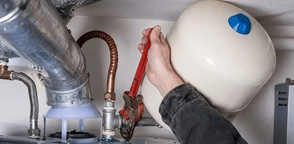 Water heater repair technician tightening plumbing connections near a tank unit in Lakewood, CO